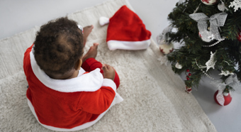 baby playing inside with Santa outfit on next to Christmas tree, high angle