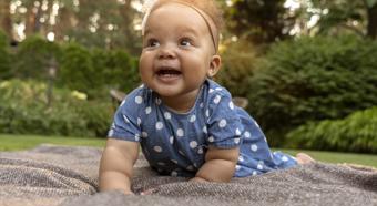 Smiley baby crawling on blanket, with a nice green nature backdrop.