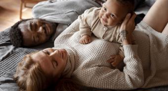 Young women and man laying on home setting floor with little baby smiling while laying on women's lap