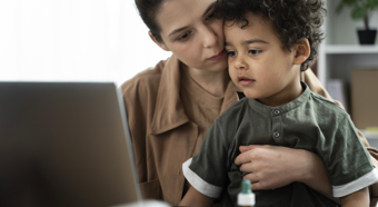 Women holding young boy in a dark green shirt on her lap, while both of them look at a laptop computer screen 